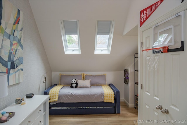 bedroom with lofted ceiling with skylight and light hardwood / wood-style flooring