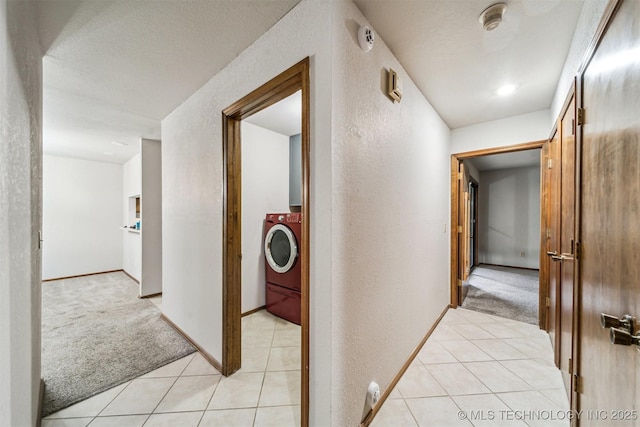 corridor with washer / clothes dryer, light carpet, and a textured ceiling