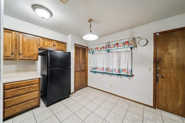 kitchen featuring black refrigerator, light tile patterned floors, hanging light fixtures, and a textured ceiling