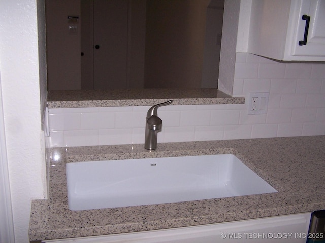 room details featuring white cabinetry, sink, and light stone counters