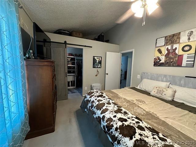 bedroom with concrete flooring, vaulted ceiling, ceiling fan, a barn door, and a textured ceiling