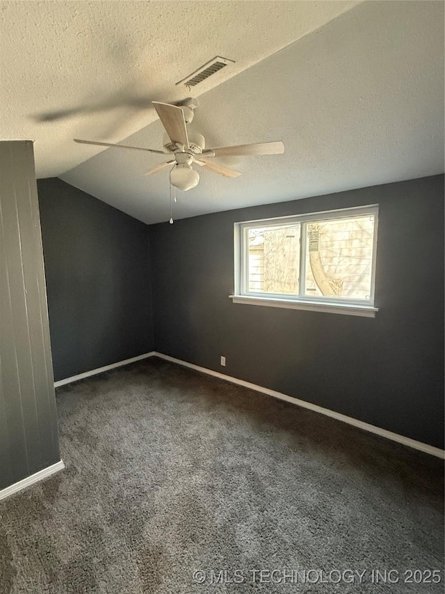 spare room featuring dark carpet, vaulted ceiling, a textured ceiling, and ceiling fan