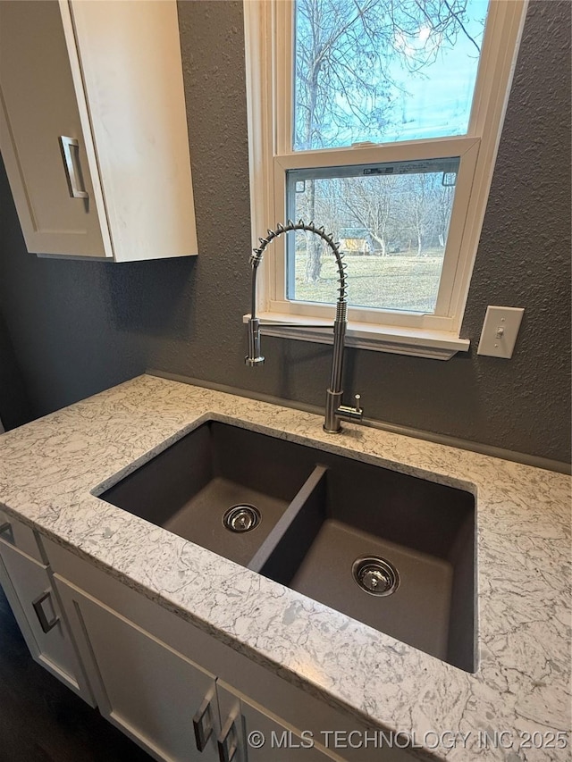 interior details with light stone counters, sink, and white cabinets