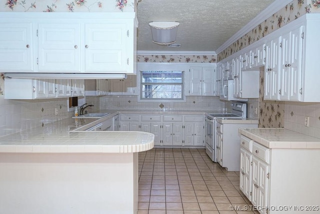 kitchen with sink, white appliances, white cabinets, tile countertops, and kitchen peninsula