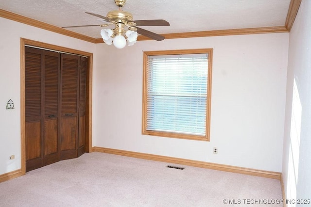 unfurnished bedroom featuring light colored carpet, ceiling fan, crown molding, a textured ceiling, and a closet