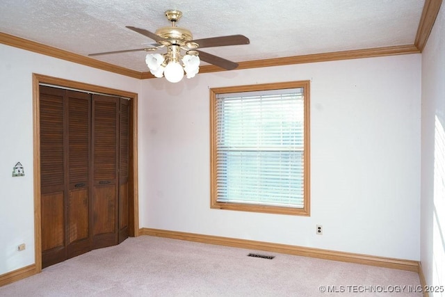 unfurnished bedroom with light colored carpet, ceiling fan, crown molding, a textured ceiling, and a closet