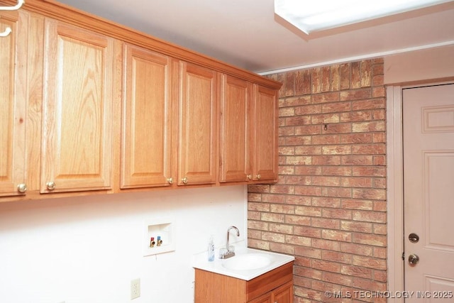 clothes washing area with washer hookup, sink, cabinets, and brick wall