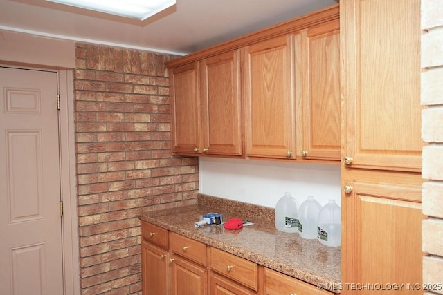 kitchen featuring light stone counters and brick wall