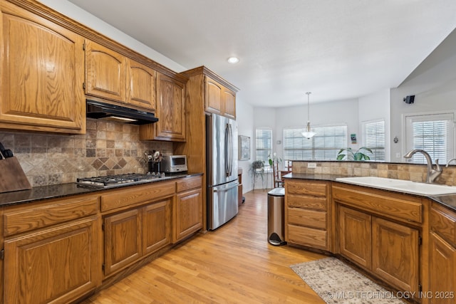 kitchen with sink, tasteful backsplash, hanging light fixtures, appliances with stainless steel finishes, and light hardwood / wood-style floors