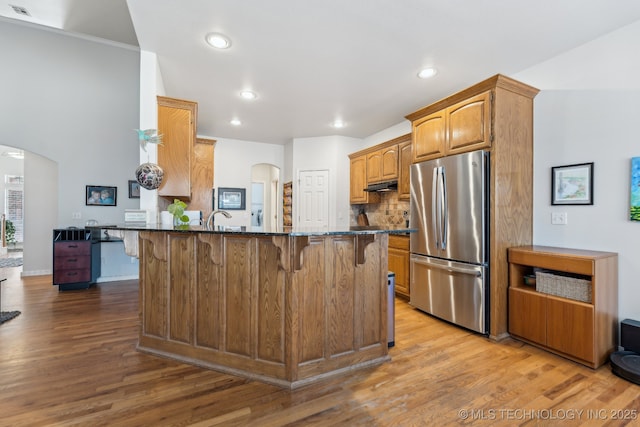 kitchen with a breakfast bar area, stainless steel fridge, kitchen peninsula, dark stone counters, and light hardwood / wood-style floors