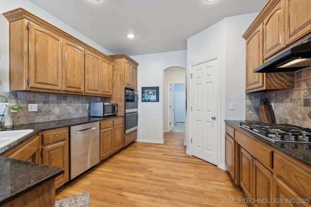 kitchen with appliances with stainless steel finishes, sink, dark stone countertops, decorative backsplash, and light hardwood / wood-style floors