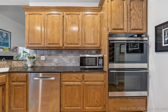 kitchen with tasteful backsplash, sink, dark stone countertops, and appliances with stainless steel finishes