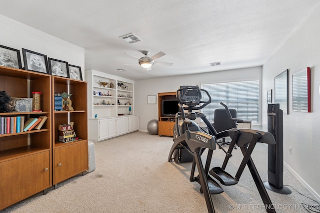 exercise area featuring a textured ceiling, light colored carpet, and ceiling fan