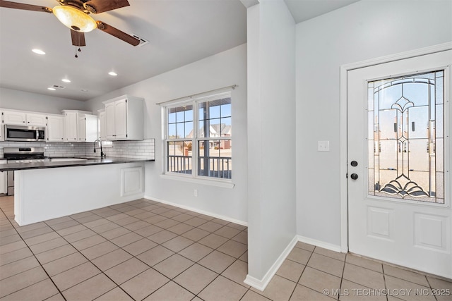 kitchen with light tile patterned flooring, kitchen peninsula, stainless steel appliances, decorative backsplash, and white cabinets