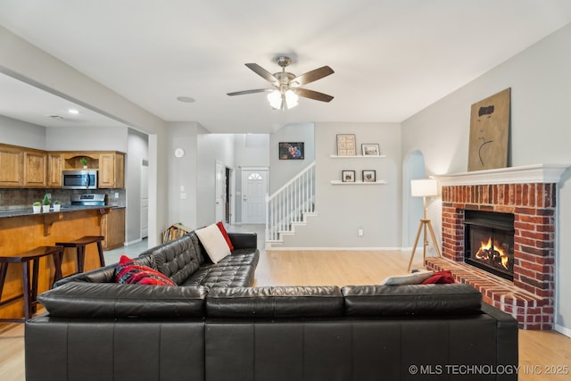 living room with a brick fireplace, ceiling fan, and light hardwood / wood-style flooring