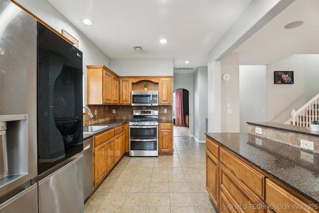 kitchen featuring sink, light tile patterned floors, dark stone countertops, appliances with stainless steel finishes, and decorative backsplash