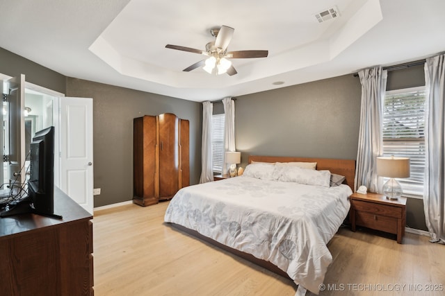 bedroom featuring light hardwood / wood-style flooring, ceiling fan, and a tray ceiling