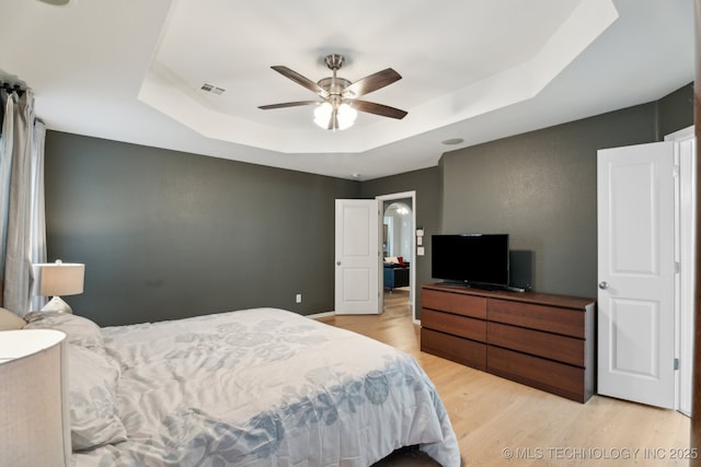 bedroom with ceiling fan, a tray ceiling, and light hardwood / wood-style floors