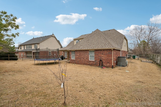 back of property featuring central AC unit, a trampoline, and a lawn