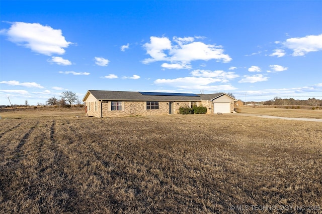 single story home featuring a garage, solar panels, a front lawn, and a rural view