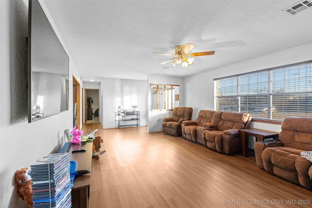 living room featuring ceiling fan, a textured ceiling, and light wood-type flooring