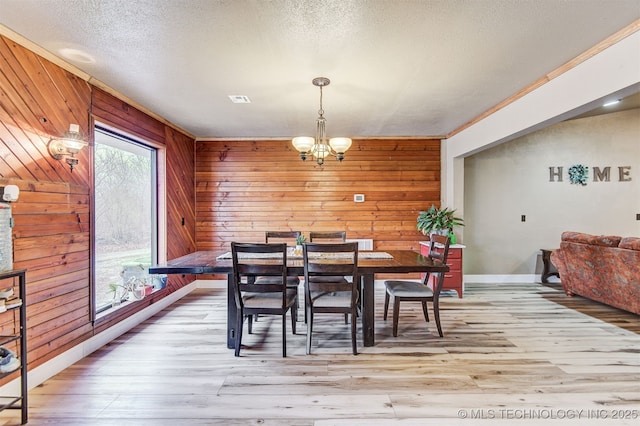 dining area featuring an inviting chandelier, light hardwood / wood-style flooring, a textured ceiling, and wood walls