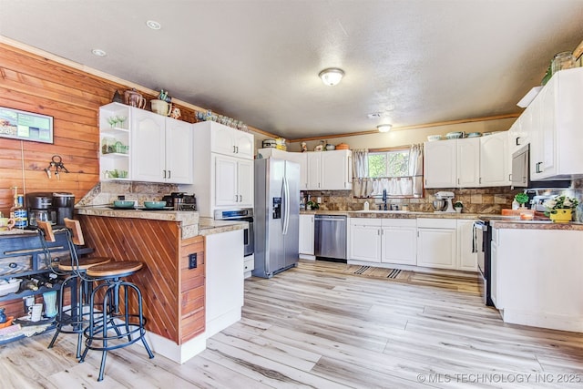 kitchen featuring a breakfast bar area, white cabinetry, stainless steel appliances, light hardwood / wood-style floors, and decorative backsplash