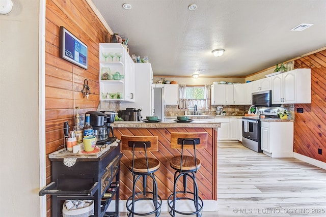 kitchen with a breakfast bar, appliances with stainless steel finishes, white cabinetry, light hardwood / wood-style floors, and wood walls