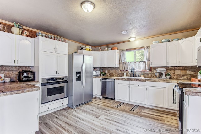 kitchen with sink, tasteful backsplash, light wood-type flooring, appliances with stainless steel finishes, and white cabinets