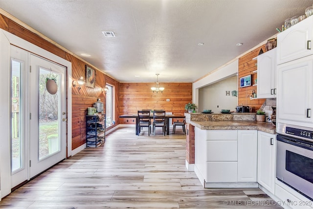 kitchen with hanging light fixtures, plenty of natural light, stainless steel oven, and white cabinets