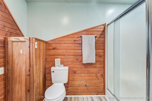 bathroom featuring toilet, hardwood / wood-style floors, wooden walls, and a shower with shower door