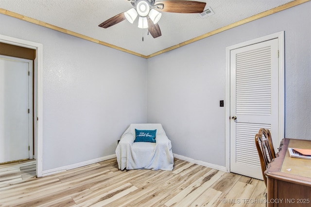 living area with ceiling fan, ornamental molding, a textured ceiling, and light wood-type flooring