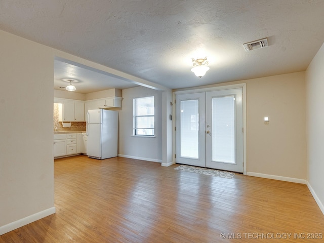 interior space with a textured ceiling, light wood-type flooring, and french doors