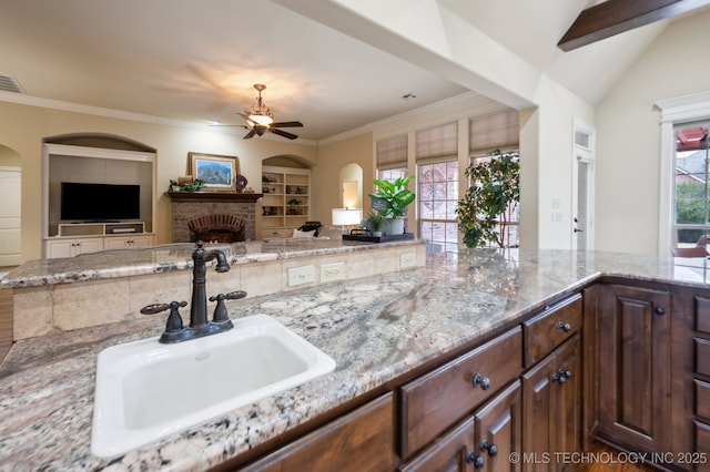 kitchen featuring sink, crown molding, built in features, light stone counters, and a fireplace