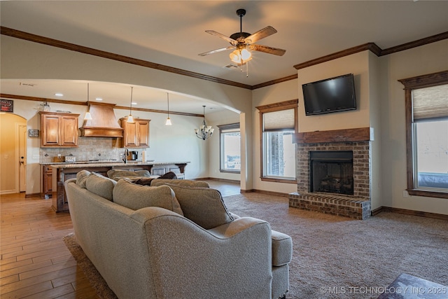 living room with crown molding, ceiling fan with notable chandelier, and a fireplace