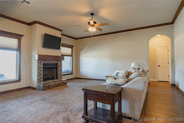 living room featuring crown molding, ceiling fan, hardwood / wood-style floors, and a brick fireplace