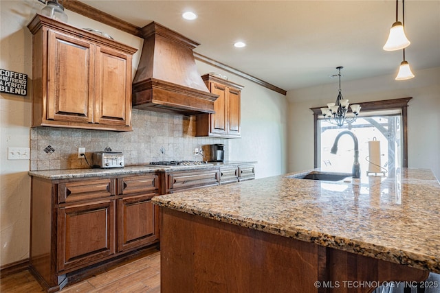 kitchen with sink, light stone counters, tasteful backsplash, decorative light fixtures, and custom exhaust hood