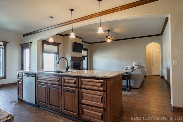 kitchen with dark hardwood / wood-style floors, decorative light fixtures, stainless steel dishwasher, a brick fireplace, and a center island with sink