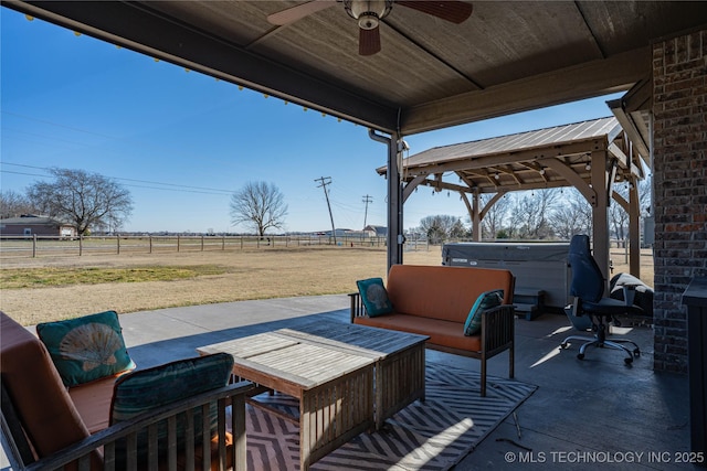 view of patio featuring ceiling fan, a hot tub, an outdoor hangout area, and a rural view