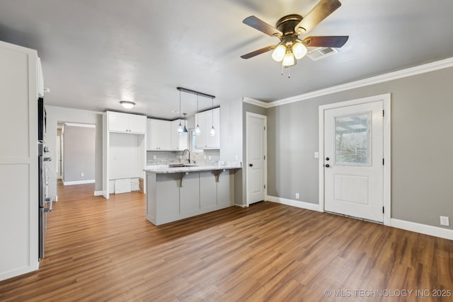 kitchen featuring a kitchen bar, sink, white cabinetry, hanging light fixtures, and kitchen peninsula