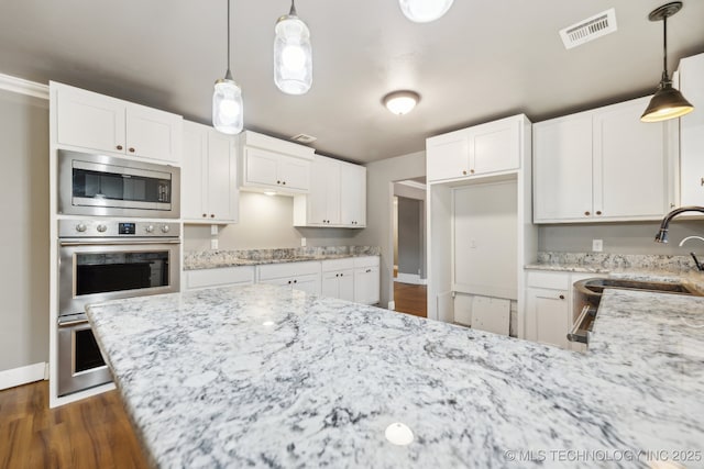 kitchen featuring light stone countertops, white cabinetry, appliances with stainless steel finishes, and pendant lighting