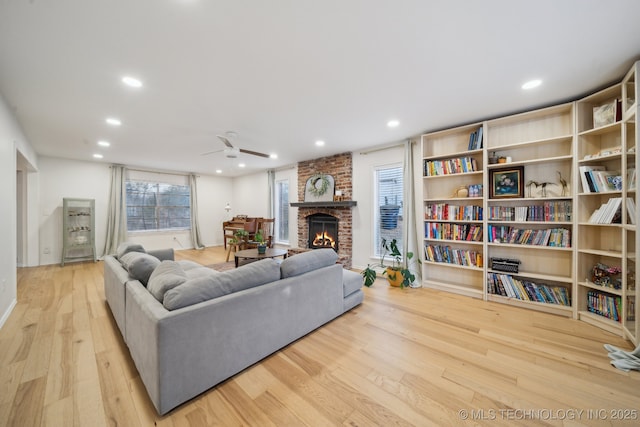 living room with ceiling fan, a brick fireplace, and light hardwood / wood-style floors