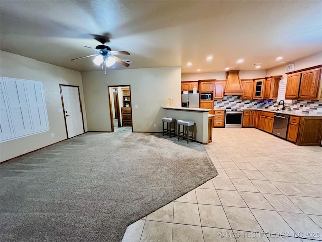 kitchen featuring a breakfast bar, backsplash, stainless steel appliances, custom range hood, and light carpet