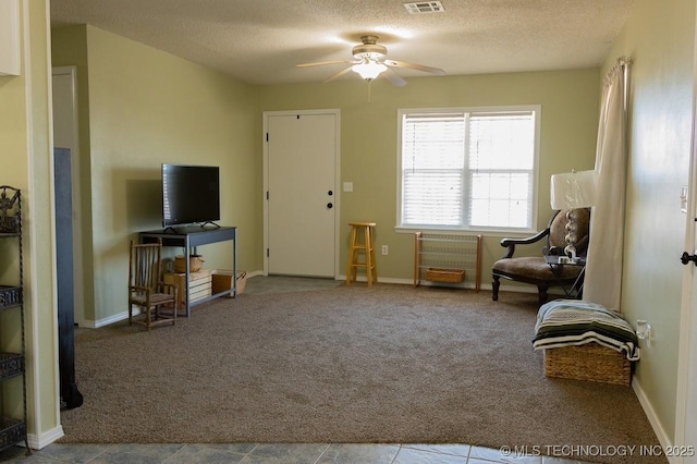 living area featuring light carpet, ceiling fan, and a textured ceiling