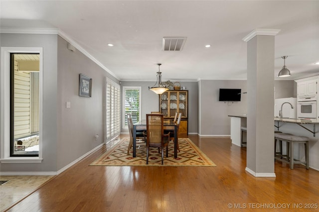 dining room featuring decorative columns, ornamental molding, wood-type flooring, and sink