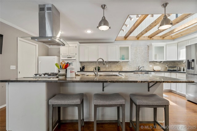 kitchen featuring white appliances, a breakfast bar, white cabinets, island exhaust hood, and dark stone counters