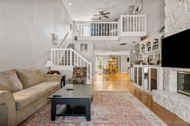 living room with ceiling fan, a stone fireplace, hardwood / wood-style floors, and a towering ceiling