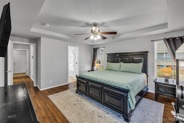 bedroom featuring a raised ceiling, ensuite bathroom, dark hardwood / wood-style floors, and ceiling fan