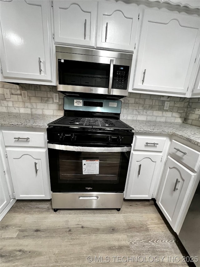 kitchen with light stone countertops, gas stove, and white cabinets