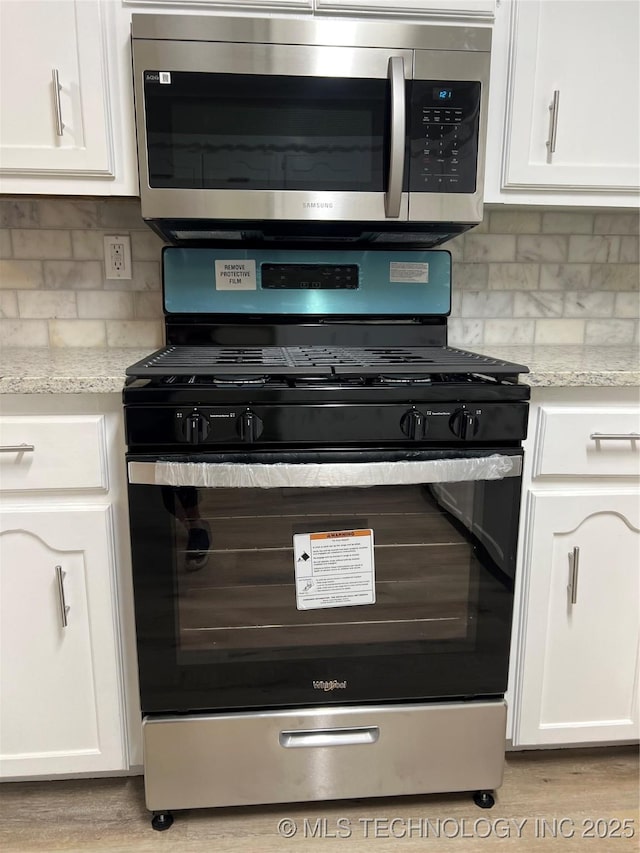 kitchen featuring gas range, tasteful backsplash, light stone counters, and white cabinets